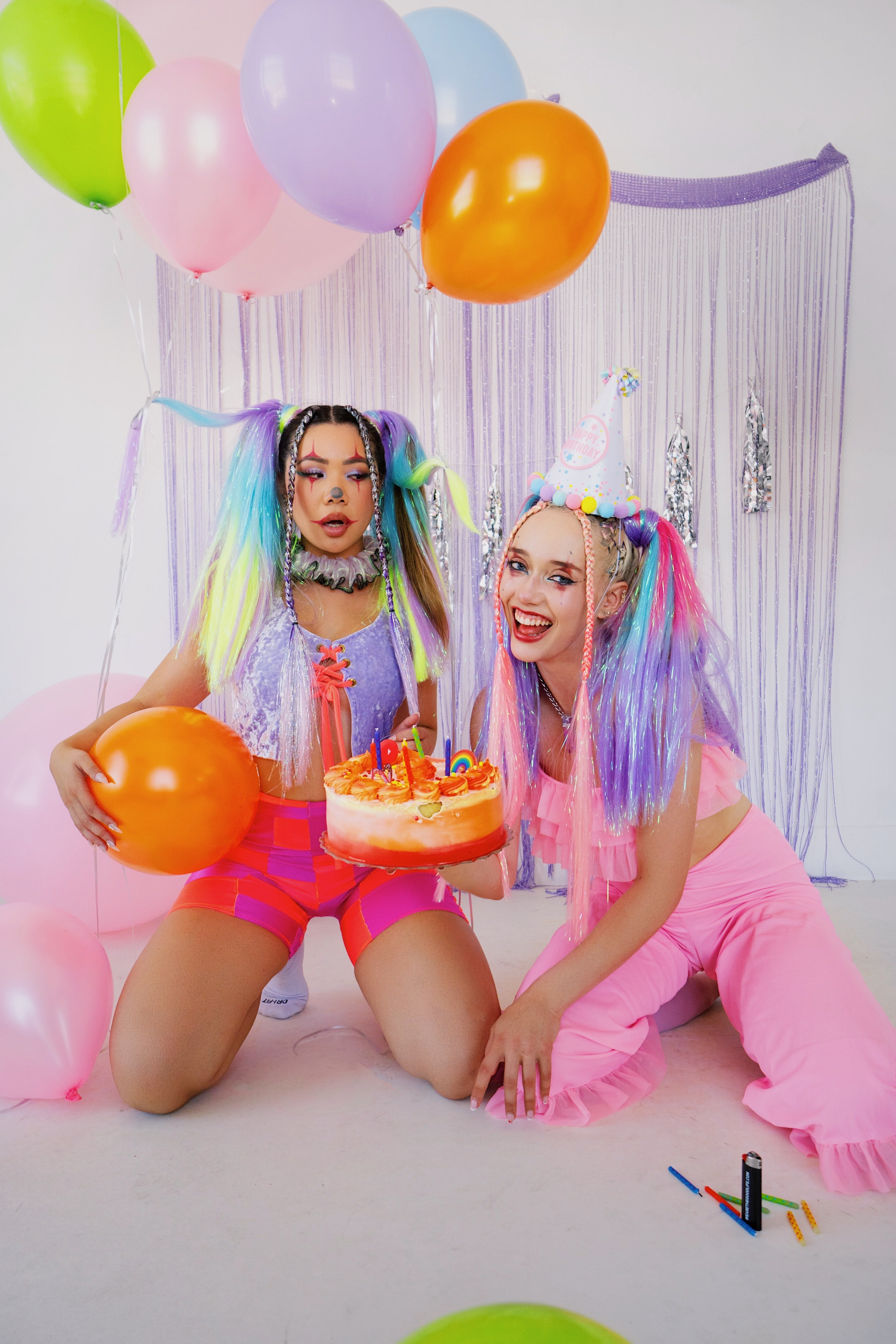 2 women dressed as clowns holding a balloon and cake