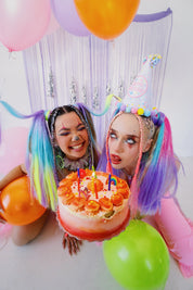 2 women in birthday rave attire holding a cake